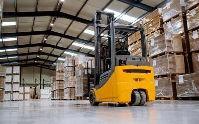 A forklift in a warehouse stacked high with palletts.